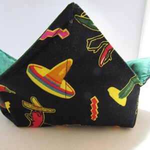 May include: A black fabric bowl with a green lining. The bowl has a Mexican-themed print with chili peppers, sombreros, and cacti.