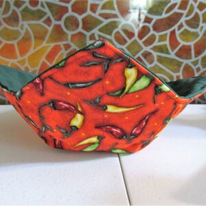 May include: A red and green fabric bowl with a chili pepper pattern. The bowl is folded and has a green lining.