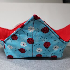 May include: A blue and red fabric bowl with a ladybug and flower pattern. The bowl is folded and ready to be used.
