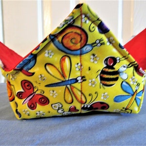 May include: A yellow fabric bowl with a red lining and a bug-themed print. The print features butterflies, ladybugs, dragonflies, bees, and snails.