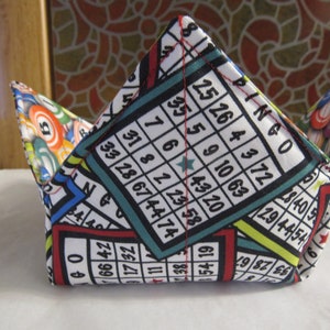 May include: A fabric bowl with a colorful bingo card pattern. The bowl is folded into a cone shape and has red, blue, green, and yellow accents.