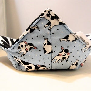 May include: A blue and white fabric bowl with a cow and milk bottle print. The bowl is folded and has a black and white zebra print on the inside.