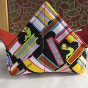 May include: A red and black fabric bowl with a book-themed print. The bowl features colorful illustrations of books, a worm, and the words "Science" and "Vol. 1".