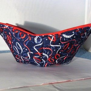 May include: A red and blue fabric bowl with a pattern of white and red ribbons on a navy blue background. The bowl is folded and has a red trim.