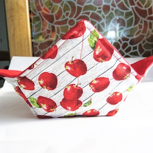 Peut inclure: Un bol en tissu rouge et blanc avec un motif de grain de bois et des pommes rouges imprimées dessus. Le bol est plié et a une doublure rouge.