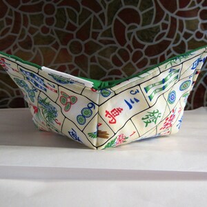 May include: A green and white fabric bowl with a Mahjong tile pattern. The bowl is folded and sitting on a white surface. The text "Pizza Creations" is visible on the bowl.