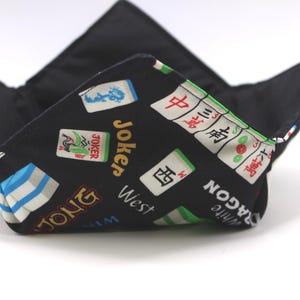 May include: Black fabric bowl with a Mahjong tile pattern. The bowl has a square shape with folded corners. The pattern includes tiles with Chinese characters, Jokers, and the word "Jong".