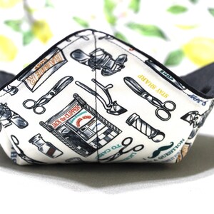 May include: A white fabric bowl with a black lining. The bowl is printed with a barber shop theme, featuring scissors, razors, and the text "Jack the Clipper".