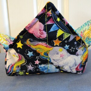 May include: A black fabric pouch with a unicorn and rainbow print. The pouch is folded into a triangular shape with a pointed top.