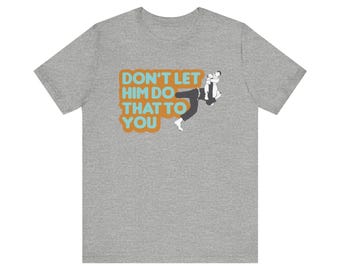 May include: A heather gray t-shirt with the text "DON'T LET HIM DO THAT TO YOU" in orange and blue. The graphic depicts a person being held upside down by another person.