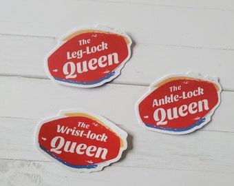 May include: Three red and white stickers with the text "The Leg-Lock Queen", "The Wrist-lock Queen", and "The Ankle-Lock Queen".