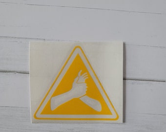 May include: Yellow warning sign with a white silhouette of two hands clasped together. The sign is a triangle with a white border.