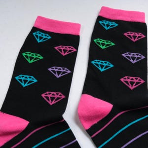 Pu&ograve; includere: Un paio di calzini neri con bordini rosa e motivi a rombi colorati.