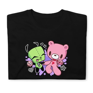 Puede incluir: Camiseta negra con un personaje de dibujos animados verde y un oso de peluche rosa con un coraz&oacute;n rojo y una huella de mano ensangrentada. Los personajes est&aacute;n rodeados de salpicaduras moradas y blancas.