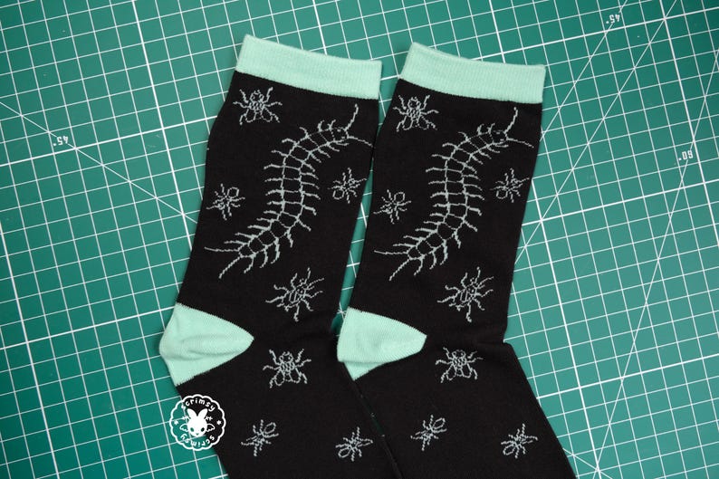 May include: A pair of black socks with a mint green cuff. The socks feature a white graphic of a centipede and small insects.