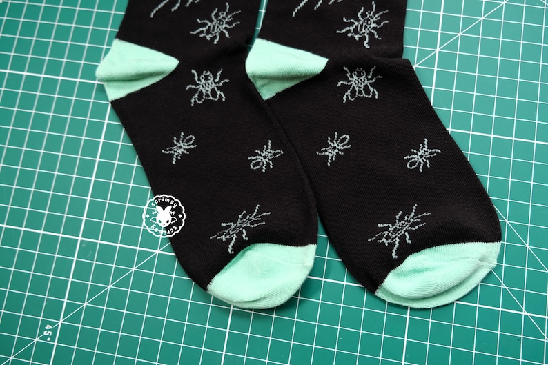 May include: A pair of black socks with a mint green heel and toe. The socks feature a repeating pattern of small, stylized ants.