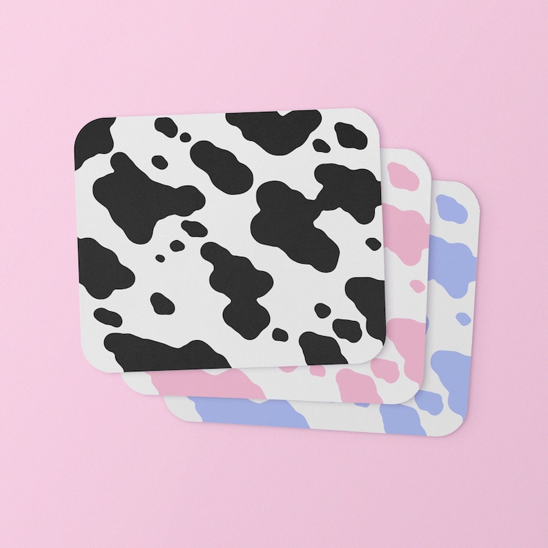May include: Three coasters with a cow print design. The top coaster is black and white, the middle coaster is pink and white, and the bottom coaster is blue and white.