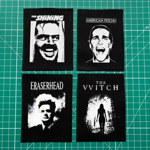 May include: Four black fabric patches with film titles and imagery. The patches feature "The Shining," "American Psycho," "Eraserhead," and "The VVitch." Each patch has a black and white image related to the film, with the title printed above.