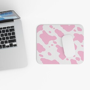 May include: A white computer mouse sits on a pink and white cow print mouse pad.