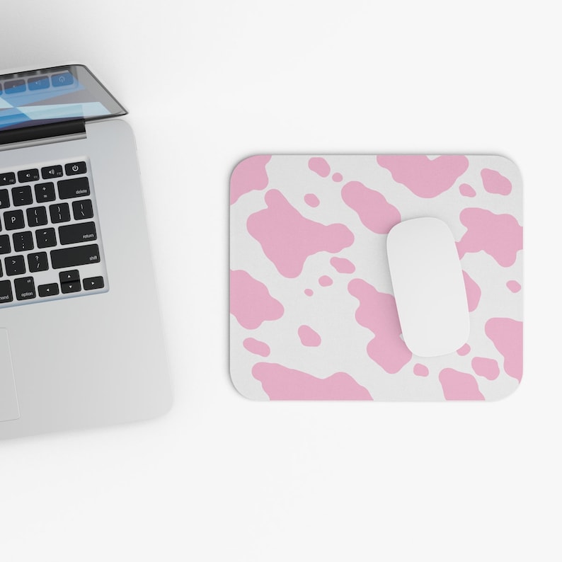 May include: A white computer mouse sits on a pink and white cow print mouse pad.