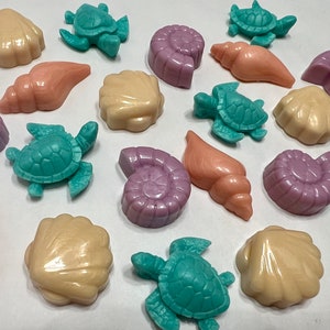 Könnte beinhalten: Eine Auswahl an farbenfrohen, dekorativen Seifenstücken in Form von Muscheln und Meeresschildkröten. Die Seifen sind in den Farbtönen Pfirsich, Lavendel, Türkis und Creme gehalten. Die Kollektion umfasst verschiedene Muschel- und Schildkröten-Designs.