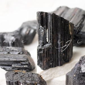 May include: A collection of black tourmaline crystals, also known as schorl, with a variety of shapes and sizes. The crystals have a dark, opaque appearance and a striated texture.