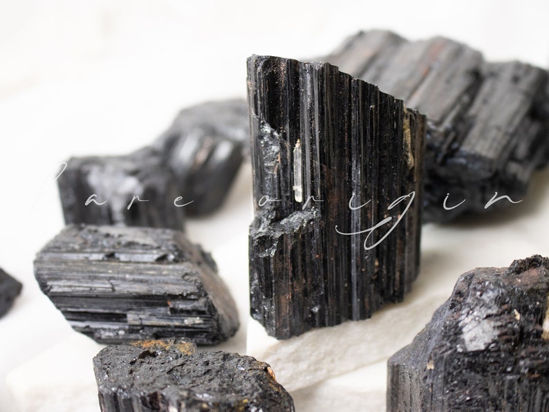 May include: A collection of black tourmaline crystals, also known as schorl, with a variety of shapes and sizes. The crystals have a dark, opaque appearance and a striated texture.