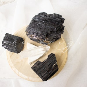 May include: Three black tourmaline crystals and a clear quartz crystal on a wooden base. The crystals are arranged in a cluster on the base.