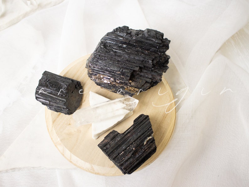 May include: Three black tourmaline crystals and a clear quartz crystal on a wooden base. The crystals are arranged in a cluster on the base.