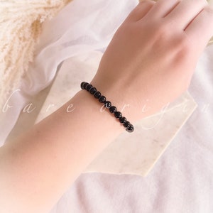May include: A black beaded bracelet on a person's wrist. The bracelet is made of small, round beads.