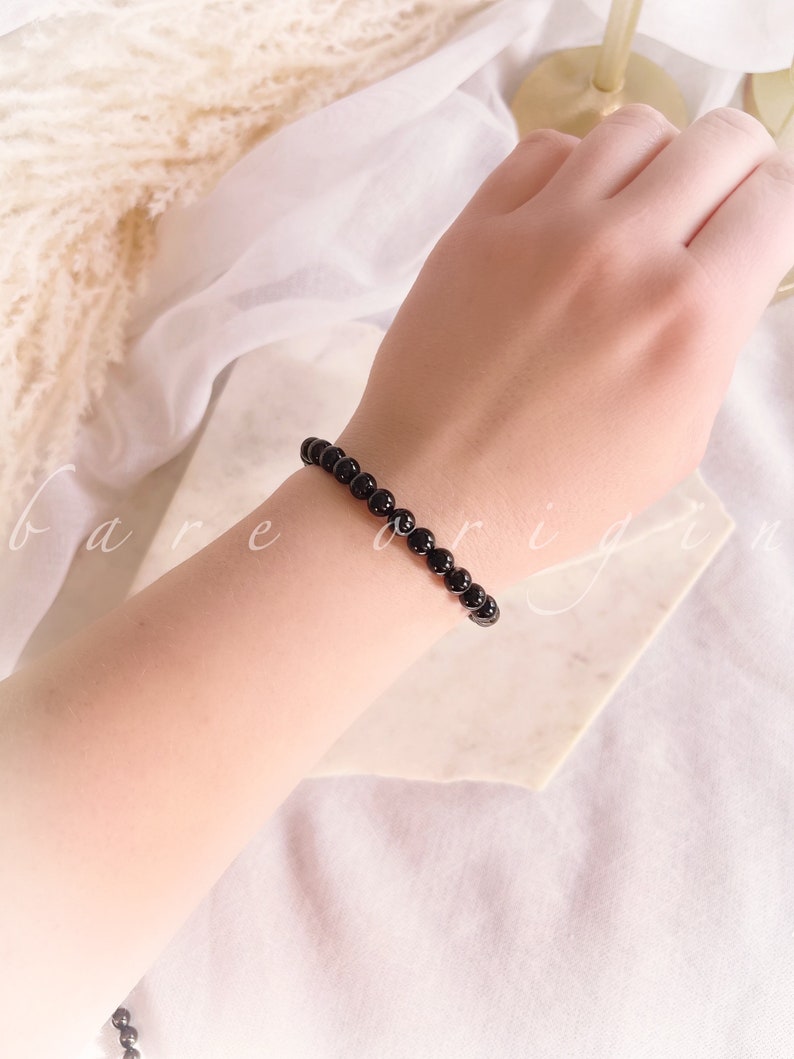 May include: A black beaded bracelet on a person's wrist. The bracelet is made of small, round beads.