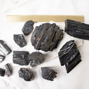 May include: A collection of black tourmaline crystals, also known as schorl, with a variety of shapes and sizes. The crystals are raw and unpolished, with a natural, rough texture.