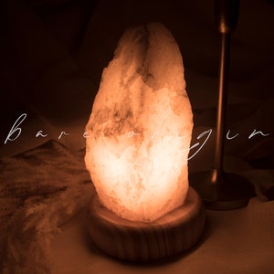 May include: A warm, glowing Himalayan salt lamp with a natural, rough-hewn shape. The lamp is on a wooden base and emits a soft, orange light.