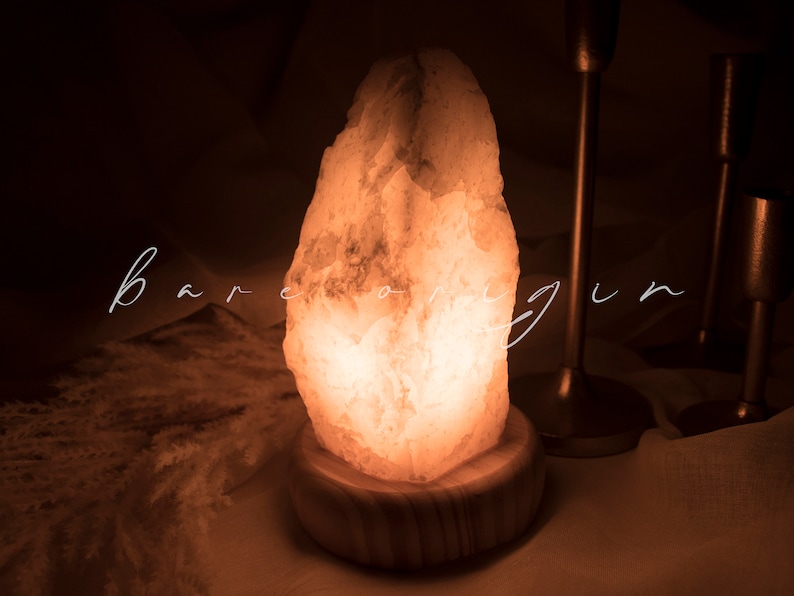 May include: A warm, glowing Himalayan salt lamp with a natural, rough-hewn shape. The lamp is on a wooden base and emits a soft, orange light.