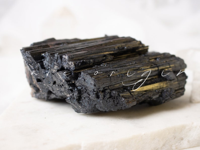 May include: A large, black, rough, and jagged piece of black tourmaline crystal. The crystal has a striated texture and a dark, almost metallic sheen.