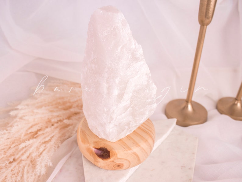 May include: A white crystal salt lamp with a wooden base. The lamp is on a white marble surface.