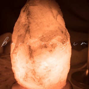 May include: A large, irregularly shaped, white Himalayan salt lamp with a warm, orange glow. The lamp is sitting on a wooden base.