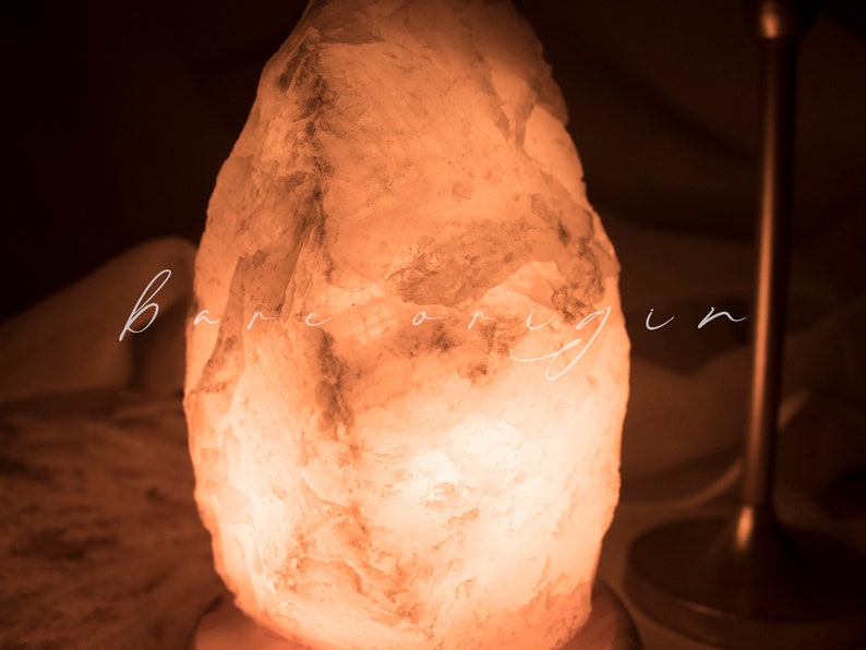 May include: A large, irregularly shaped, white Himalayan salt lamp with a warm, orange glow. The lamp is sitting on a wooden base.
