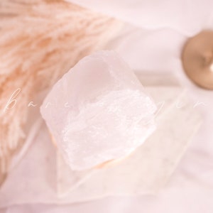 May include: A large, clear quartz crystal on a white pedestal. The crystal is smooth and polished, with a natural, irregular shape.