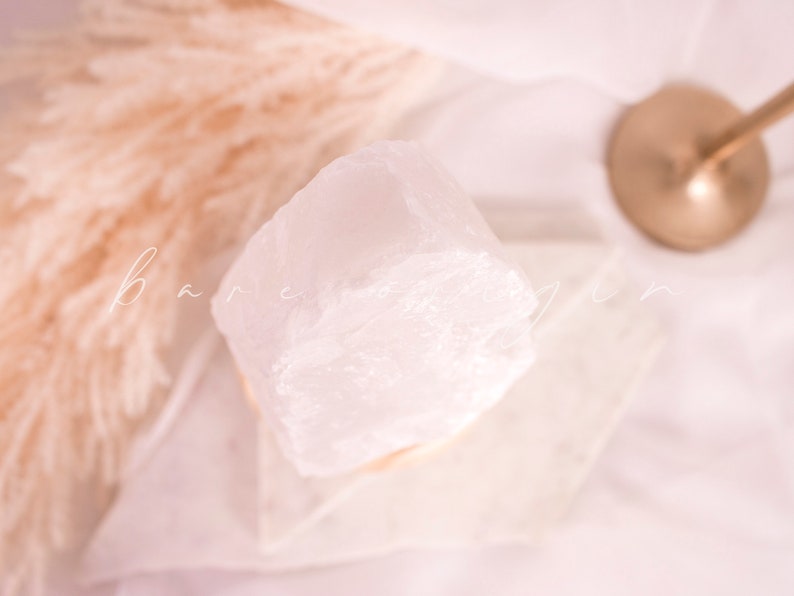 May include: A large, clear quartz crystal on a white pedestal. The crystal is smooth and polished, with a natural, irregular shape.