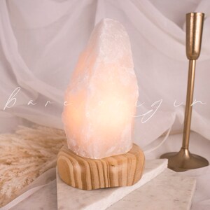 May include: A white Himalayan salt lamp with a wooden base. The lamp is lit and glowing.