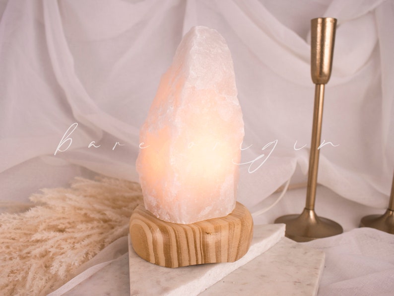 May include: A white Himalayan salt lamp with a wooden base. The lamp is lit and glowing.