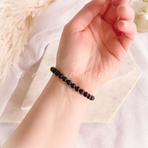 May include: A black beaded bracelet on a person's wrist. The bracelet is made of small, round beads.