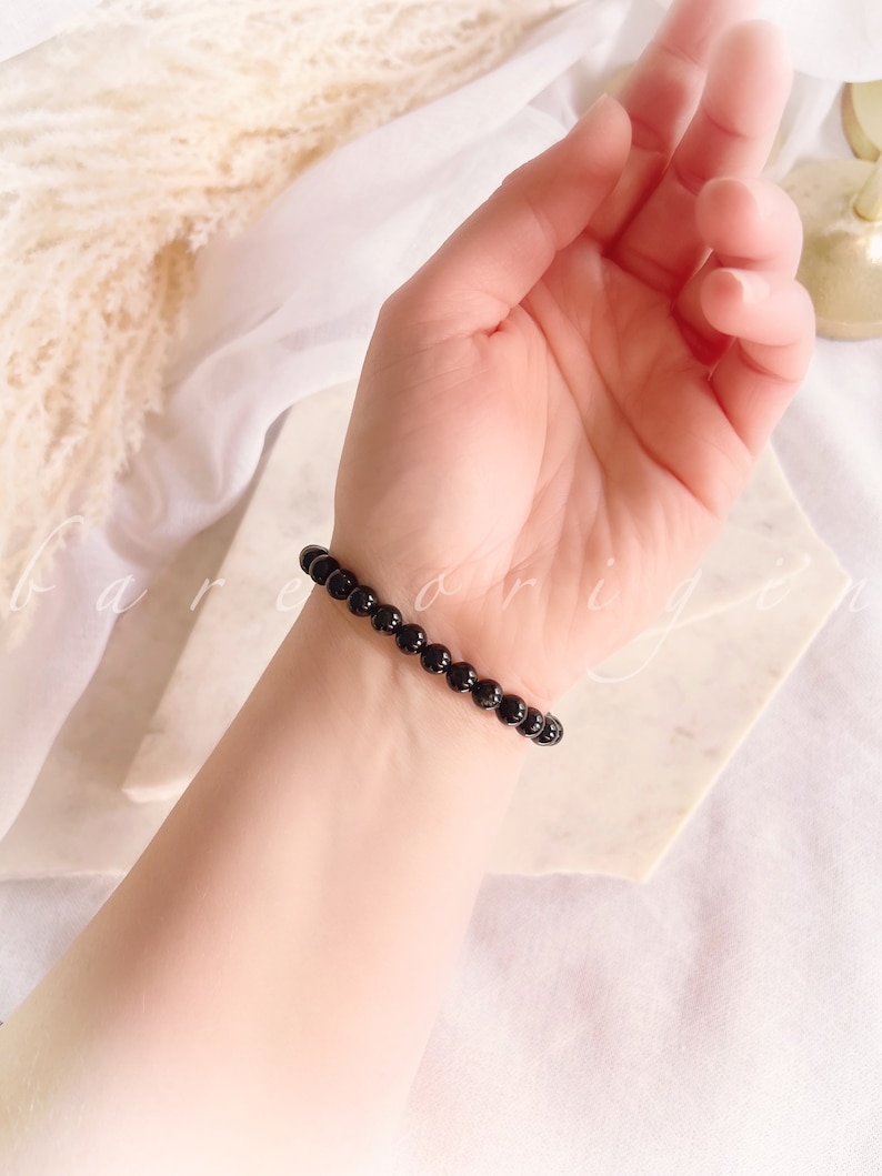 May include: A black beaded bracelet on a person's wrist. The bracelet is made of small, round beads.
