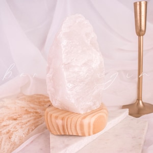 May include: A white crystal lamp with a wooden base. The crystal is shaped like a large, irregular rock. The lamp is sitting on a white marble surface.