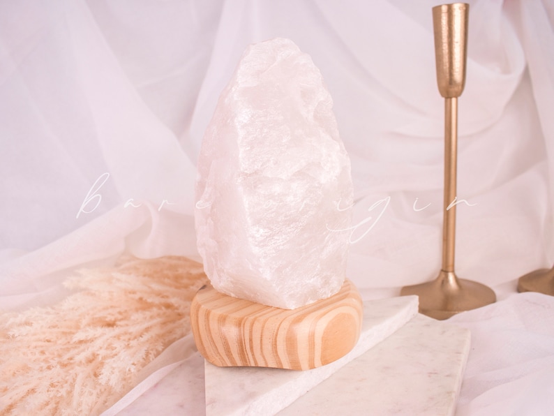 May include: A white crystal lamp with a wooden base. The crystal is shaped like a large, irregular rock. The lamp is sitting on a white marble surface.