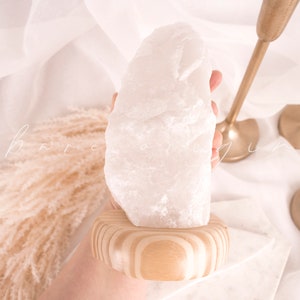 May include: A large, white, natural crystal sits on a wooden base. The crystal is rough and has a natural, organic shape.