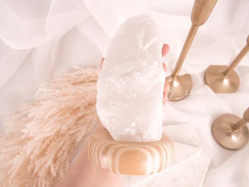 May include: A large, white, natural crystal sits on a wooden base. The crystal is rough and has a natural, organic shape.