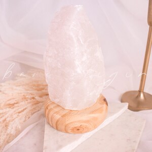 May include: A white crystal lamp with a wooden base. The lamp is sitting on a white marble surface.