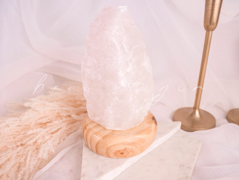 May include: A white crystal lamp with a wooden base. The lamp is sitting on a white marble surface.